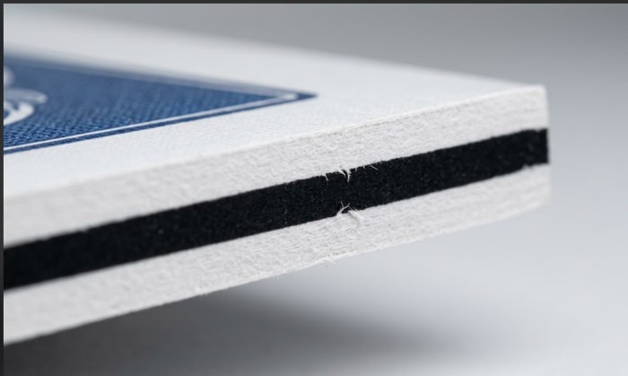 Extreme macro cross-section of 330gsm German Black Core card stock, revealing the dense black graphite center layer sandwiched between premium white paper for ultimate durability.